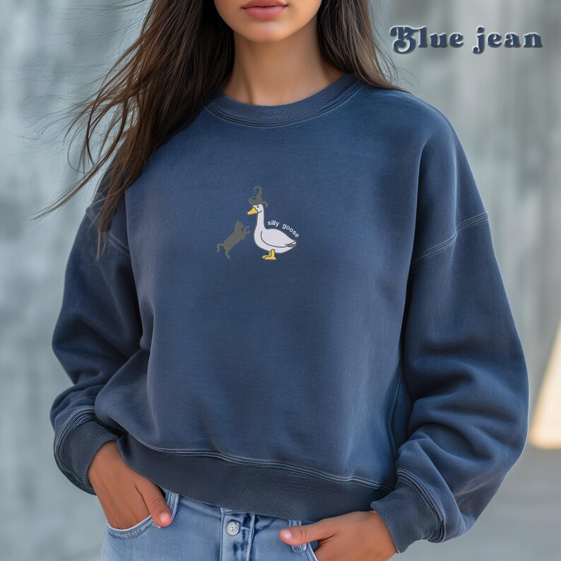 May include: A blue jean sweatshirt with a white goose and a black cat graphic on the front. The graphic says "silly goose".