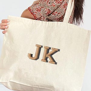 May include: A large, off-white canvas tote bag with brown embroidered letters "JK" on the front.