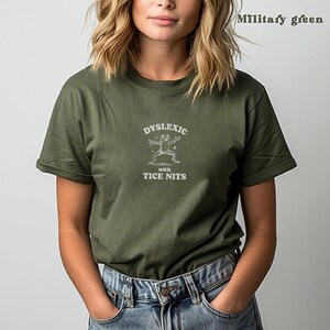 Peut inclure: Un t-shirt vert avec un graphique blanc d'une grenouille et le texte "Dyslexic with Tice Nits".