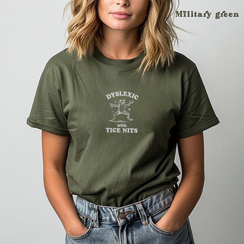 Peut inclure: Un t-shirt vert avec un graphique blanc d'une grenouille et le texte "Dyslexic with Tice Nits".
