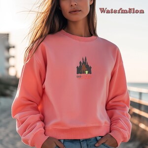 May include: A pink sweatshirt with a graphic of a castle and a figure holding a small green figure. The text "Dadalorian" is below the graphic with the words "This is the way".