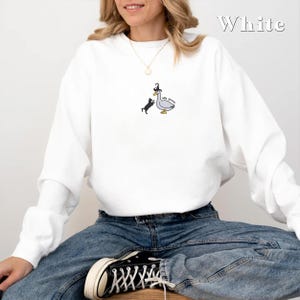 May include: White sweatshirt featuring a black cat and a goose wearing a witch's hat. The goose has the text "Silly Goose" written on it.