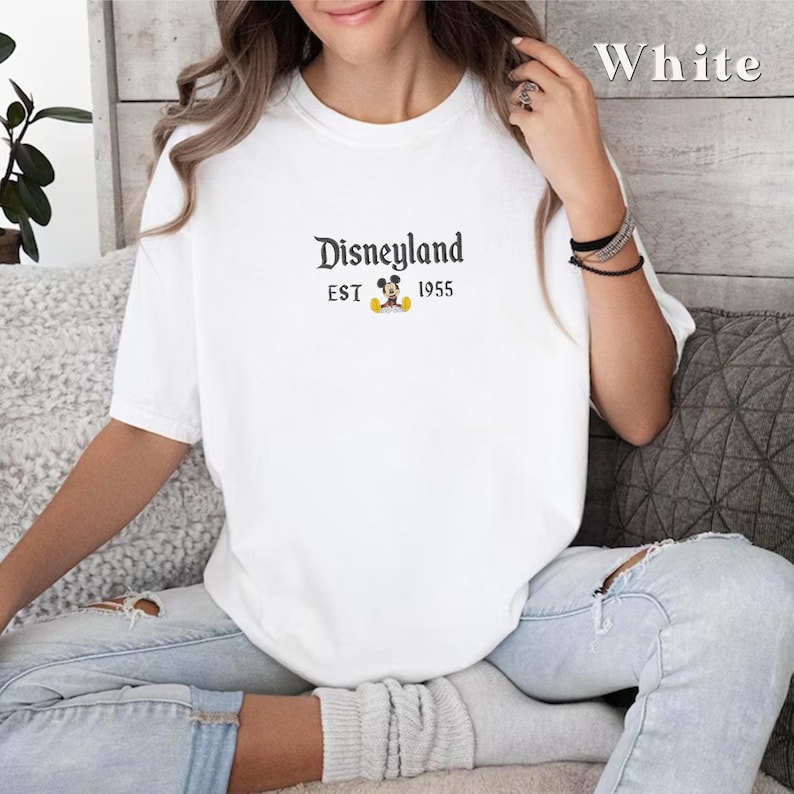 Puede incluir: Camiseta blanca con un gr&aacute;fico negro de Mickey Mouse y el texto "Disneyland EST 1955".