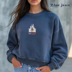 May include: A blue sweatshirt with a white graphic of a castle and a figure holding a sword. The text "The Dadalorian" and "This is the way" are printed below the graphic.