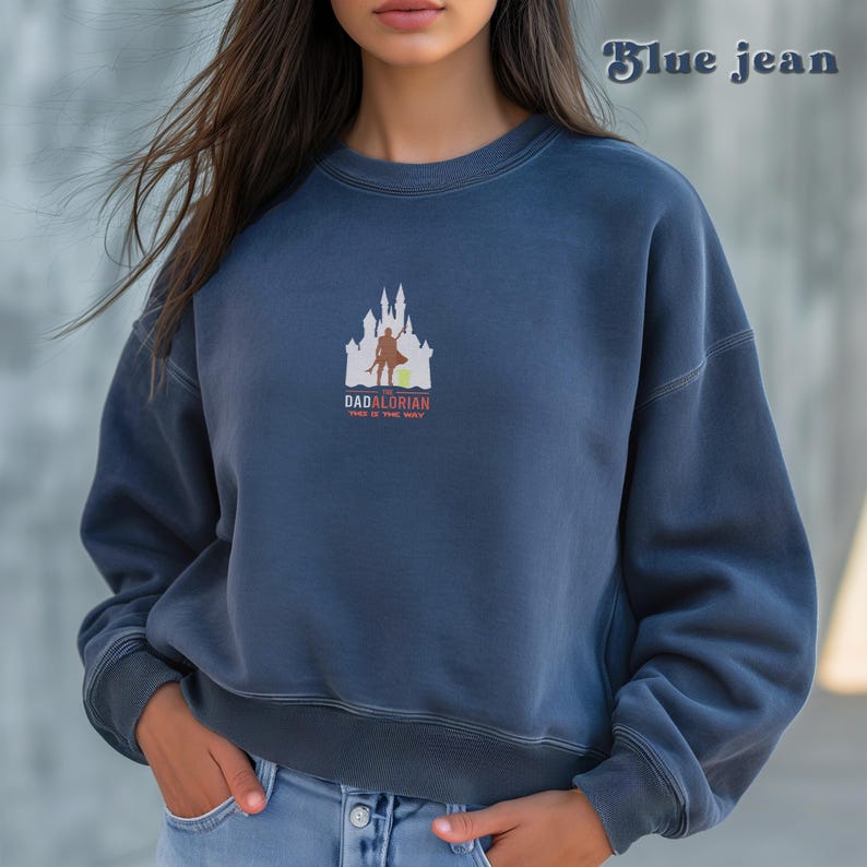 May include: A blue sweatshirt with a white graphic of a castle and a figure holding a sword. The text "The Dadalorian" and "This is the way" are printed below the graphic.
