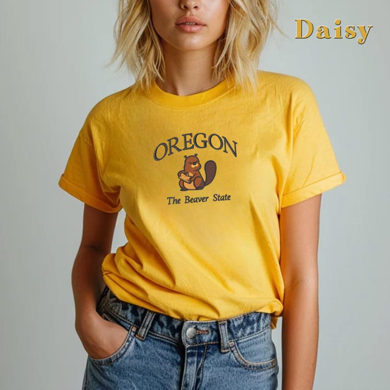 以下が含まれることがあります： 黄色のTシャツに、茶色の漫画のビーバーと「OREGON The Beaver State」の文字が書かれています。