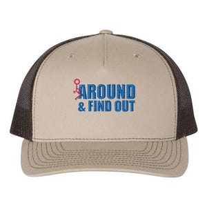 Pu&ograve; includere: Un cappello da camionista marrone e nero con il testo "AROUND & FIND OUT" ricamato in blu sul davanti. Il testo &egrave; accompagnato da un piccolo omino rosso.