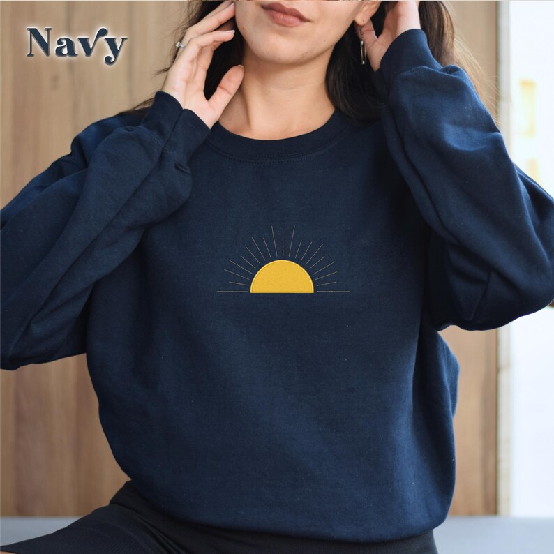 May include: A navy blue sweatshirt with a yellow sun graphic. The sun has rays coming out of it.