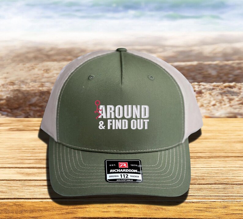 Pu&ograve; includere: Un cappello da camionista verde e bianco con il testo "AROUND & FIND OUT" ricamato sul davanti. Il cappello &egrave; regolabile e ha un logo Richardson sul retro.