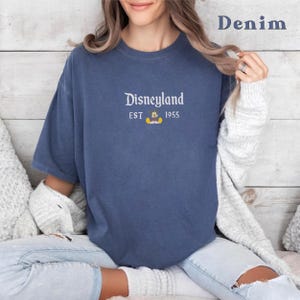 Puede incluir: Una camiseta azul denim con un gr&aacute;fico blanco que dice "Disneyland Est 1955" con un peque&ntilde;o Mickey Mouse.