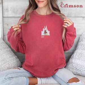 May include: A crimson red sweatshirt with a white silhouette of a castle and a figure holding a lightsaber. The text "Dad I'm Your Yoda" is printed below the image.