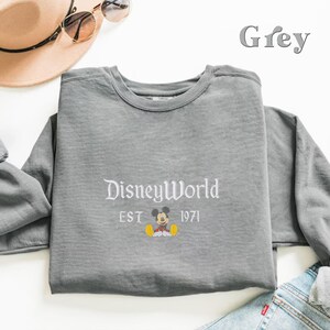 May include: Grey long-sleeve sweatshirt with a white graphic of Mickey Mouse sitting down with the text "Disney World Est 1971" underneath.
