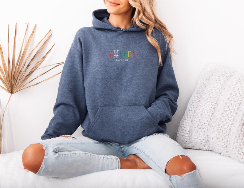 May include: A blue hoodie with a front pocket and a hood. The word "Wickey" is embroidered in colorful letters above a small graphic, with "SINCE 1928" below. The hoodie is made of a soft material.