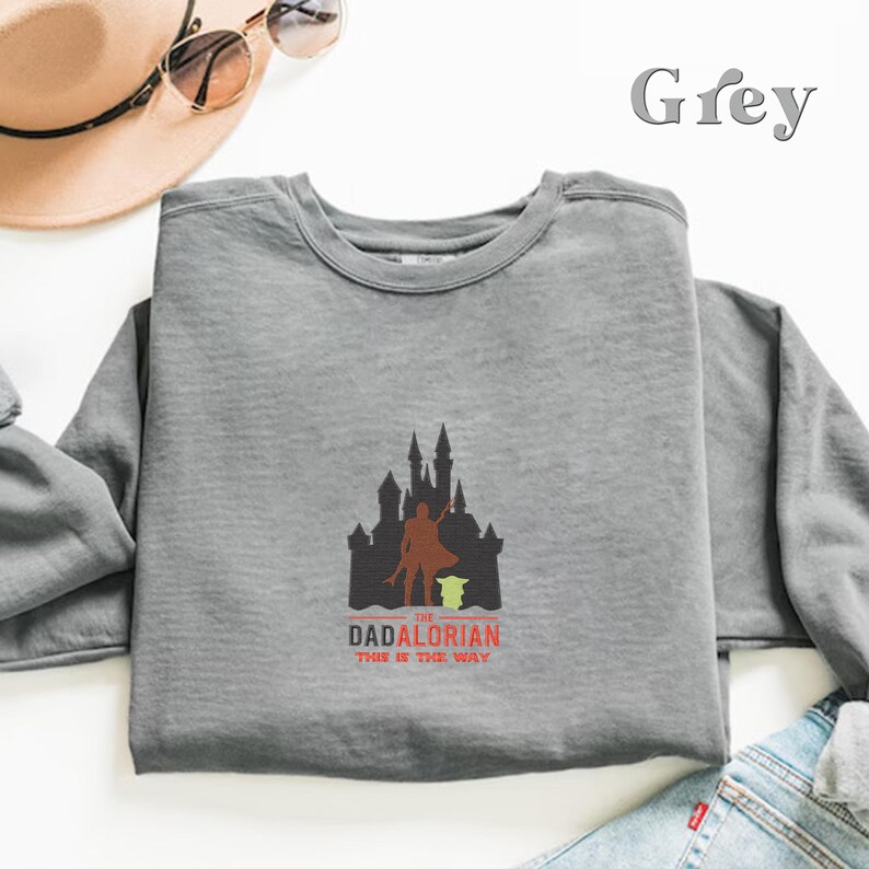 May include: Grey sweatshirt with a graphic of a castle, a figure holding a lightsaber, and the text "The Dadalorian This is the Way".