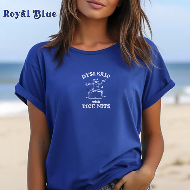 Peut inclure: Un t-shirt bleu royal avec un graphique blanc d'une grenouille et le texte "Dyslexic with Tice Nits".