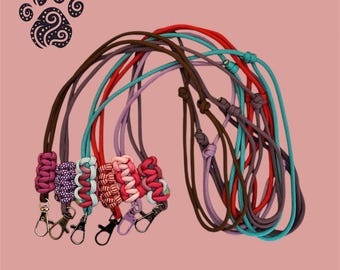 Könnte beinhalten: Eine Sammlung von sechs Schlüsselbändern aus buntem Paracord in den Farben Rot, Braun, Lila, Pink und Türkis. Jedes Band verfügt über einen geflochtenen Abschnitt und einen Karabinerhaken aus Metall. Ein dunkles Pfotenabdruck-Logo ist oben zu sehen.