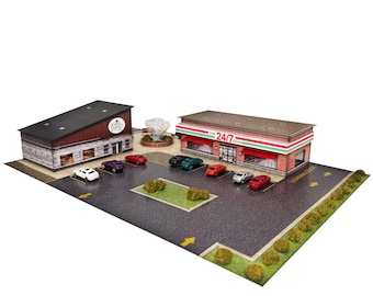 May include: A miniature diorama featuring a brick-style convenience store labeled 24/7 GRAB and an adjacent building with a dark roof. The scene includes a paved parking lot with painted yellow arrows, small toy cars, and green landscaping elements.