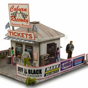 Puede incluir: Un modelo en miniatura de una taquilla de Coburn Raceway con techo a rayas, que presenta letreros de entradas, entrada y varios patrocinadores de carreras. La estructura incluye figuras pequeñas, un cajero automático y una valla con anuncios.