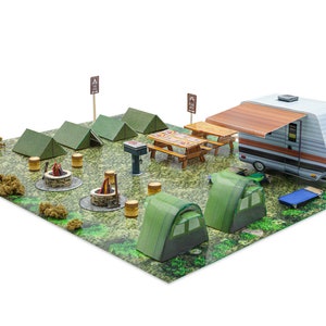 Puede incluir: Un modelo de papel en miniatura de un camping con una caravana, tiendas de campaña, mesas de picnic y una fogata. El letrero dice "Camp Alexander".