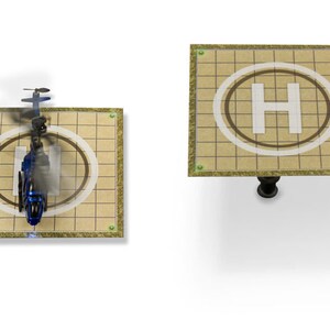 May include: A blue toy helicopter landing on a beige helipad with a white 'H' in a brown circle. The helipad has a grid pattern.