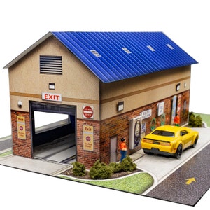 May include: A detailed model car wash with a blue corrugated roof, tan walls, and brickwork. The model features an open exit bay, a yellow car, and miniature figures. Signs read "EXIT", "$1.00 Vacuum" and "Free Air".