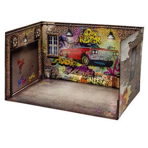 May include: A miniature diorama display set featuring a brick garage interior with a roll-up door, a window, and graffiti art on the walls. The artwork includes a red car, the text "LOW RIDER" and "MUSIC", and two hanging pendant lights.