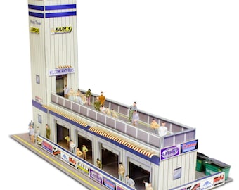 May include: A model of a race track building with a tower that says "Earl's" and "Welcome Race Fans". The building has several garage doors and a balcony with miniature people standing on it. The building is made of cardboard and has a white and blue color scheme.