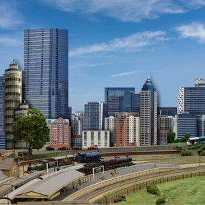 May include: A model train set with a blue and black locomotive, several passenger cars, and a train station. The train is on a track that runs through a miniature city with skyscrapers, buildings, and trees.