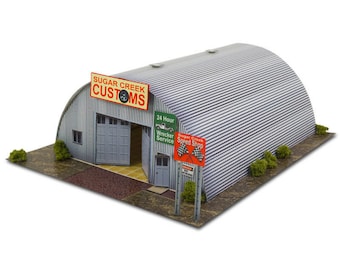 May include: A model of a corrugated metal garage with a curved roof. The garage has a sign that reads "Sugar Creek Customs" and another sign that reads "24 Hour Wrecker Service". There is a sign that reads "Sugar Creek Speed Shop" with checkered flags.