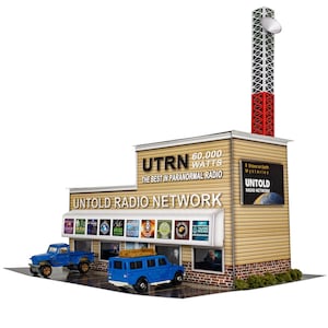 May include: A model of a radio station building with a large sign that reads "UTRN 60,000 WATTS THE BEST IN PARANORMAL RADIO UNTOLD RADIO NETWORK". The building is brown with a white awning and a red and white radio tower.