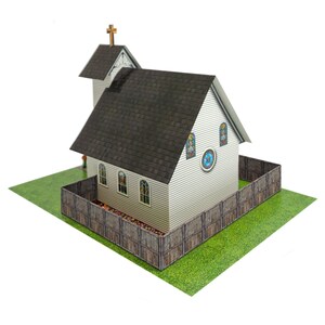May include: A miniature white church model with a dark gray roof and a small steeple topped with a gold cross. The church has stained glass windows and is surrounded by a wooden fence on a green base.