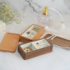 May include: Two wooden ring boxes with velvet interiors. One box is light brown and the other is dark brown. Both boxes are open and filled with rings.