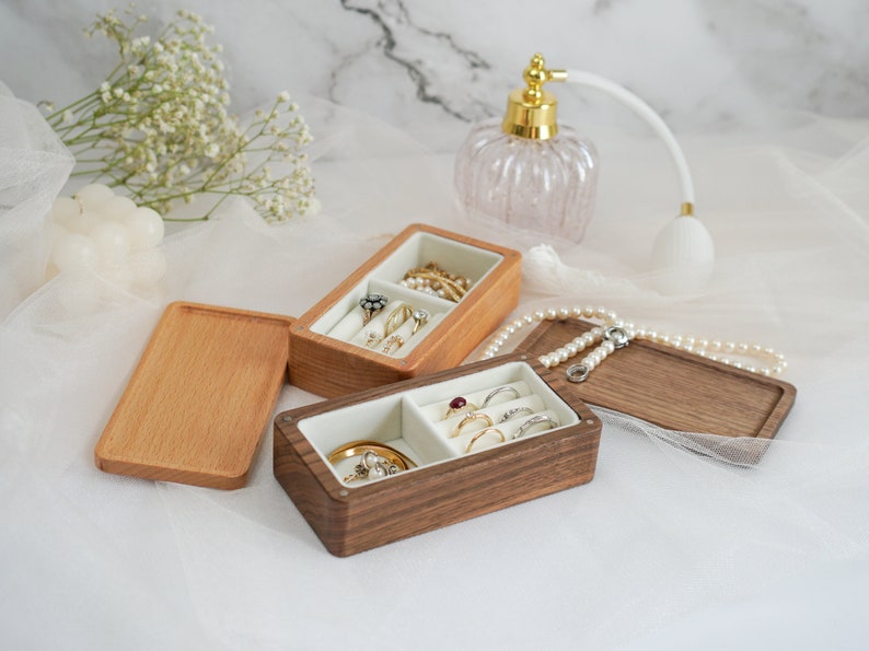 May include: Two wooden ring boxes with velvet interiors. One box is light brown and the other is dark brown. Both boxes are open and filled with rings.