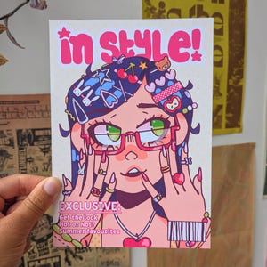 May include: A rectangular art print featuring a stylised illustration of a person with dark hair, wearing red-rimmed glasses and numerous hair clips, rings, and a heart necklace. The text reads in style! EXCLUSIVE: Get the look Hot or Not? Summer favourites.