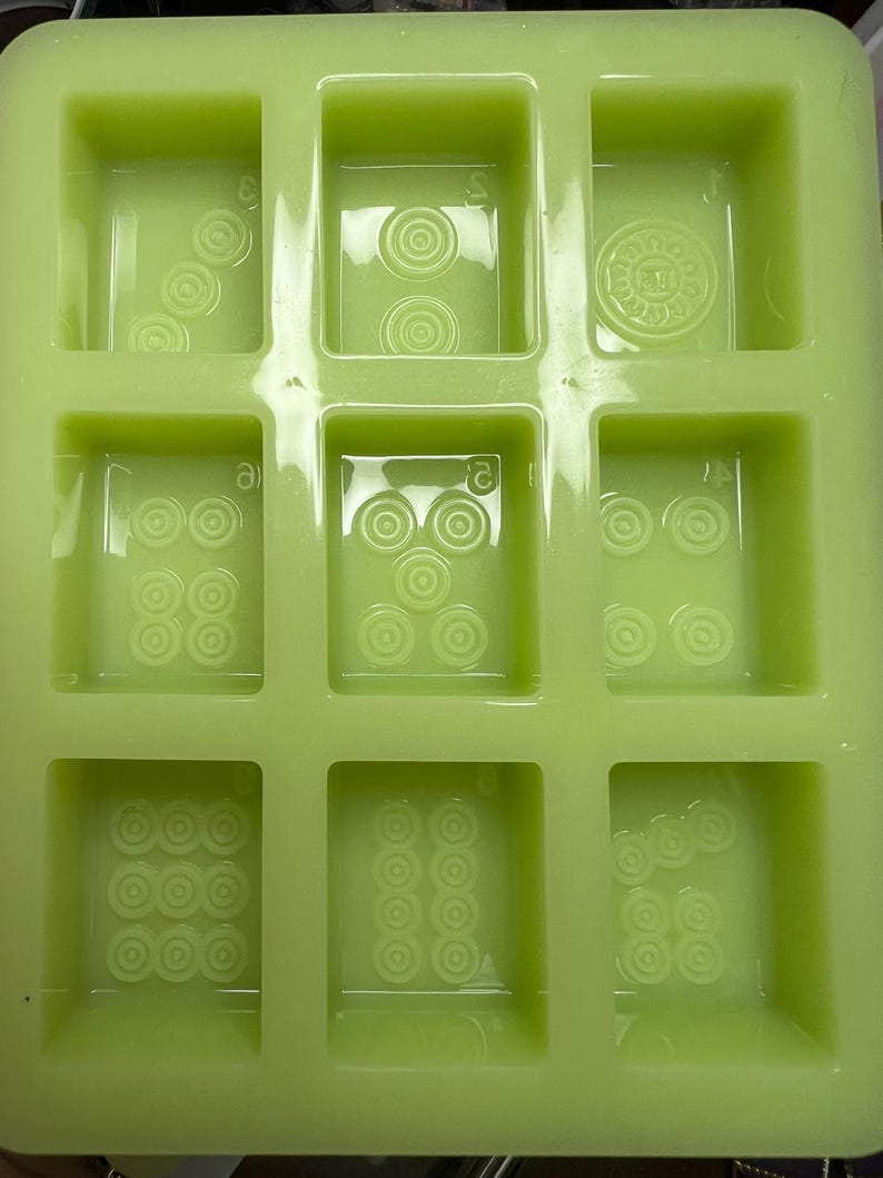 May include: Green silicone mold with nine rectangular cavities. Each cavity has a raised design of multiple circles.