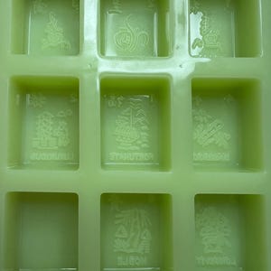 May include: A green silicone mold with nine square compartments. Each compartment has a raised design of a Chinese character. The characters are:  "福", "禄", "寿", "喜", "财", "吉", "祥", "和", "顺".