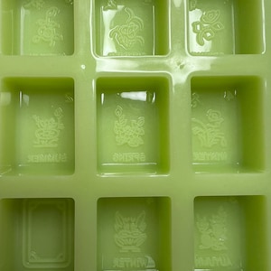 May include: Green silicone mold with nine square compartments. Each compartment has a raised design of a flower and the word "Spring", "Summer", "Winter", or "Autumn".