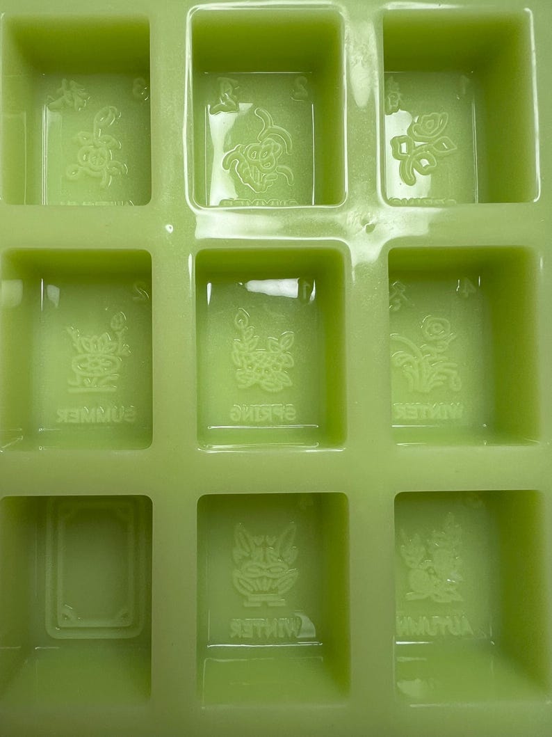May include: Green silicone mold with nine square compartments. Each compartment has a raised design of a flower and the word "Spring", "Summer", "Winter", or "Autumn".