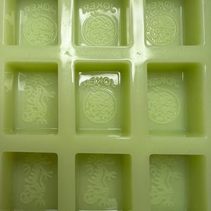 May include: Green silicone mold with six rectangular cavities. Each cavity has a raised design of a dragon with the word "JOKER" written above it.