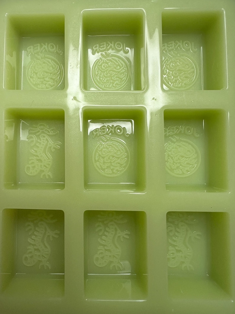 May include: Green silicone mold with six rectangular cavities. Each cavity has a raised design of a dragon with the word "JOKER" written above it.