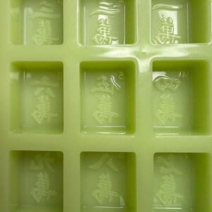 May include: A green silicone mold with nine rectangular cavities. Each cavity has a raised design of Chinese characters. The characters are "發財"