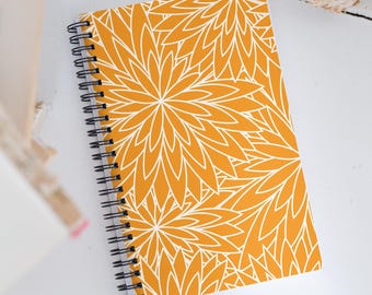 May include: A yellow spiral bound notebook with a white floral pattern. The notebook has a modern design and is perfect for taking notes, journaling, or sketching.