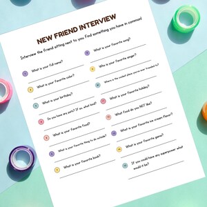 Puede incluir: Un papel blanco titulado "NEW FRIEND INTERVIEW" con preguntas para hacer a un amigo. El papel está rodeado de coloridos rollos de cinta washi en tonos de azul, rosa, verde y naranja, sobre una superficie azul claro.