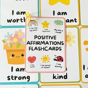 May include: A set of colourful flashcards with positive affirmations for children. Each card features a different illustration, such as a flower, a sun, a ladybug, and a heart. The cards include phrases like "I am strong", "I am worthy", and "I am loved".