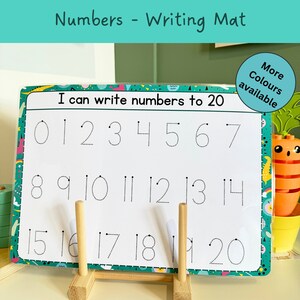 May include: A white dry-erase writing mat with a green and blue border. The mat has dotted lines for tracing numbers 0-20. The text "I can write numbers to 20" is at the top of the mat. The mat is on a wooden stand.