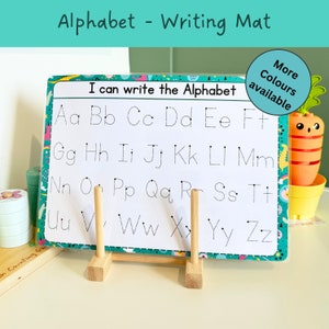 May include: A white dry-erase alphabet writing mat with a colorful border and dotted lines for tracing letters. The mat is on a wooden easel stand. The text on the mat reads "I can write the Alphabet".