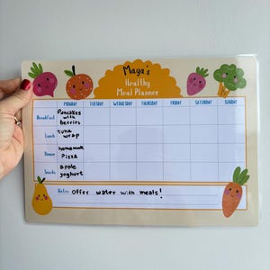 Puede incluir: Un planificador de comidas beige con el texto "Maya's Healthy Meal Planner" y un horario semanal. El planificador presenta ilustraciones de frutas y verduras. El horario incluye secciones de desayuno, almuerzo, cena y meriendas.