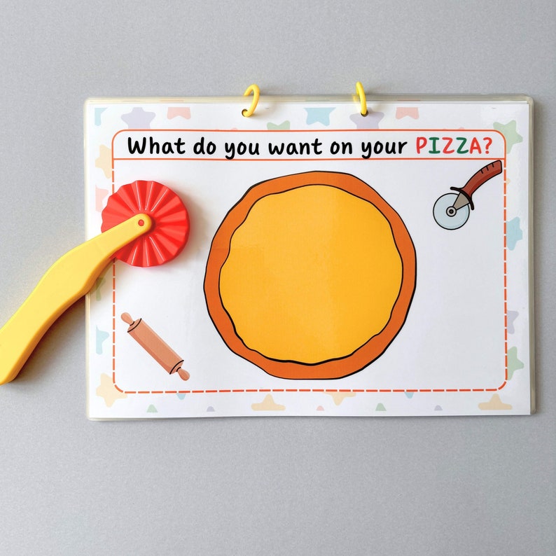 May include: A children's pizza-themed activity board with the text "What do you want on your PIZZA?". The board features a pizza base illustration, a pizza cutter, a rolling pin, and a pizza wheel. The board is bound with yellow rings.
