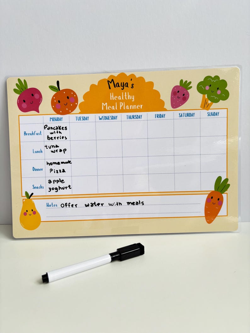 Puede incluir: Un planificador de comidas amarillo y blanco con el texto "Maya's Healthy Meal Planner". El planificador tiene una cuadr&iacute;cula para las comidas diarias, con ilustraciones de frutas y verduras. Un marcador blanco y negro est&aacute; delante del planificador.