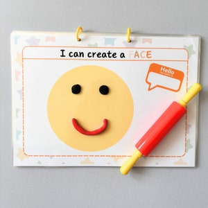 May include: A children's activity set with the text "I can create a FACE". The set includes a yellow smiley face with black eyes and a red smile made of clay. A red and yellow rolling pin is also included.